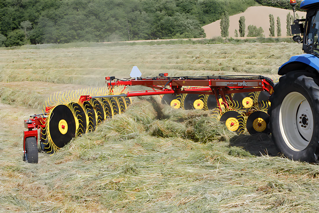Ein Traktor zieht einen V-förmigen Fingerrad-Heurechen durch dickes, geerntetes Stroh