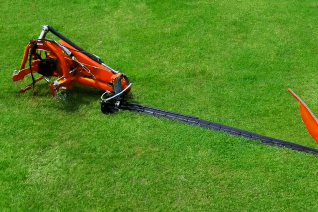 Tractor-mounted single-blade lawn mower clearing dense overgrowth in a field