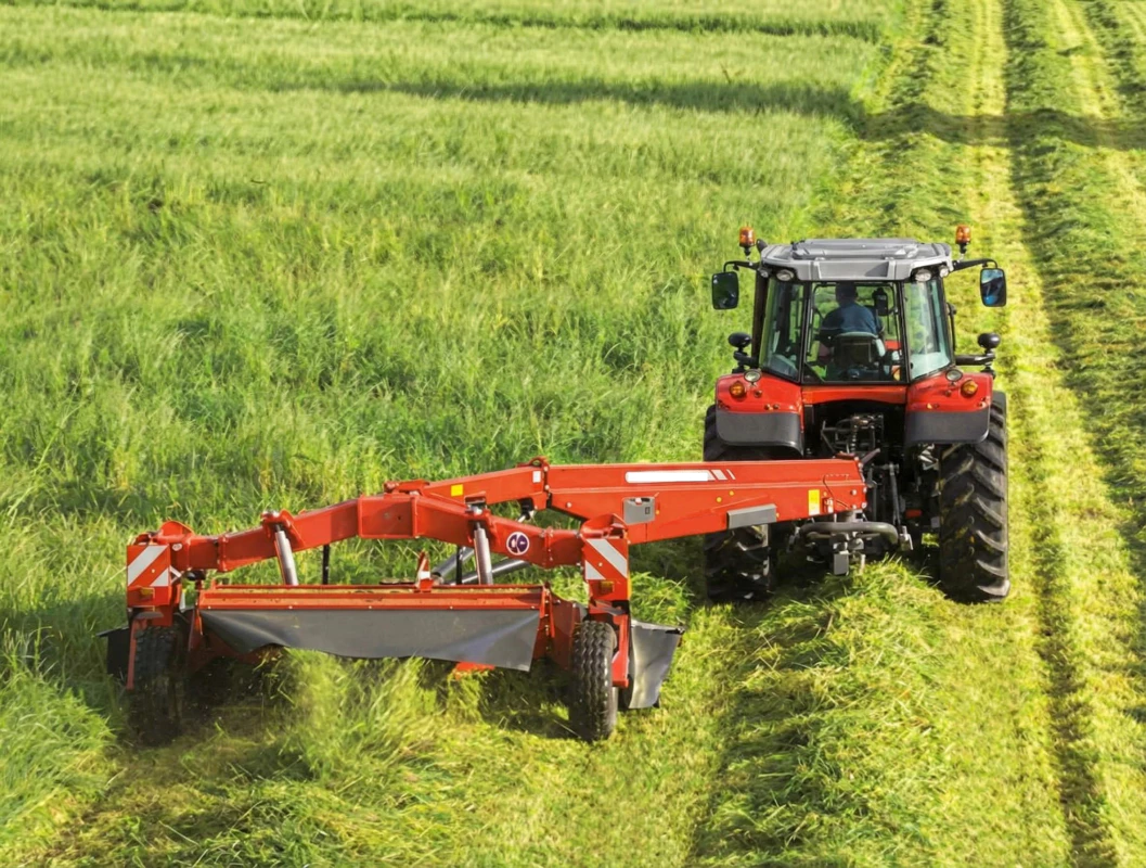Tractor pulling a rotary disc mower conditioner through a farm field